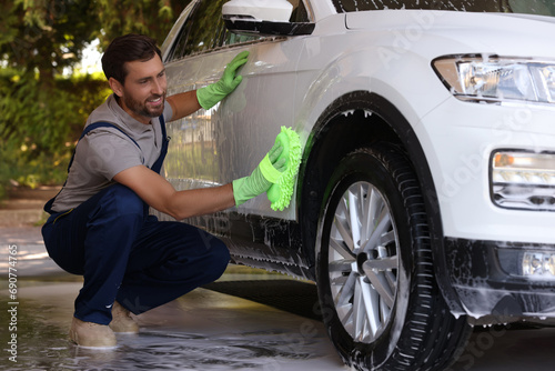 Worker washing auto with sponge at outdoor car wash