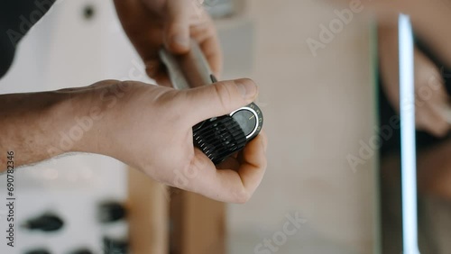 Hand holding an electric hair clipper with an adjustable guard, set against a blurred background, suggesting a grooming or haircutting scenario. photo