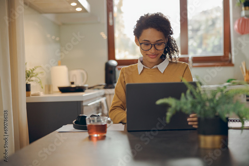 Smiling female manager working remotely on laptop from home while sitting near window