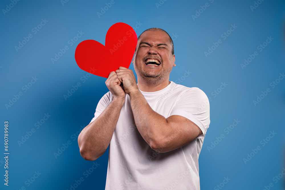 man holding a paper heart with both hands, at face level, laughing with his eyes closed man holding a paper heart with both hands, at face level, laughing with his eyes closed