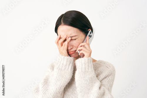 スマホで通話をしながら泣く中年女性　白背景 photo