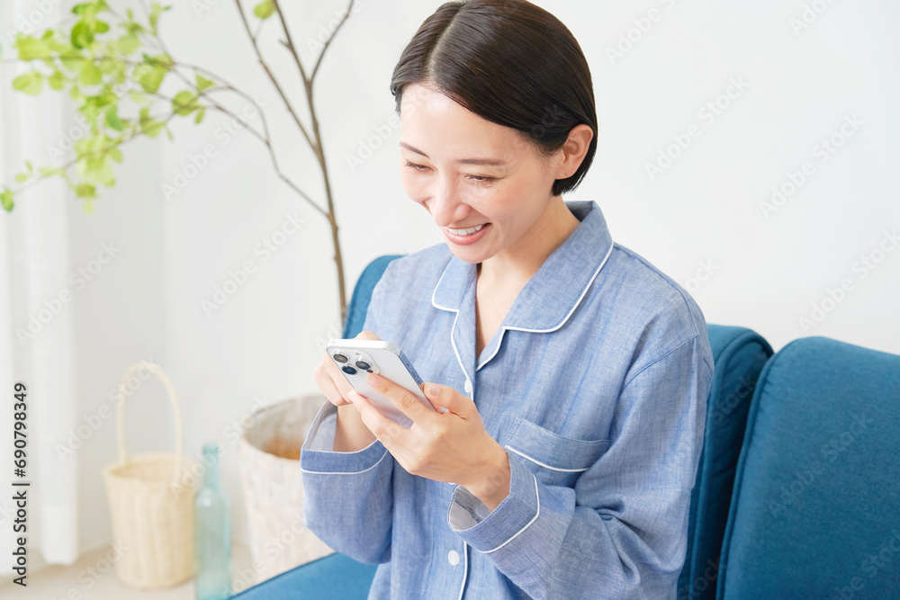 自宅でパジャマを着てスマホを使う中年女性 自宅でパジャマを着てスマホを使う中年女性