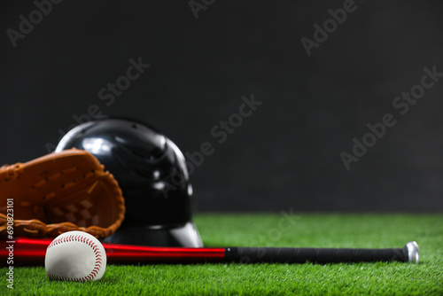 Photography Baseball bat, batting helmet, leather glove and ball on green grass against dark background