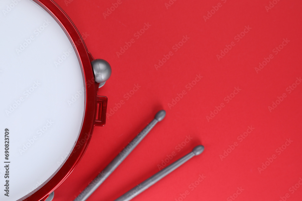 Drum and sticks on red background, top view with space for text. Percussion musical instrument Drum and sticks on red background, top view with space for text. Percussion musical instrument