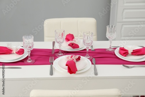 Color accent table setting. Glasses, plates, cutlery and pink napkins in dining room