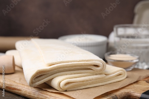 Raw puff pastry dough on wooden table, closeup photo
