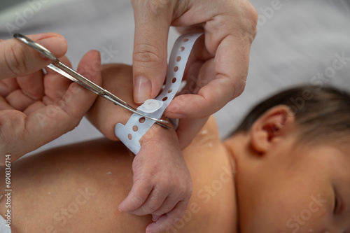 A woman cuts a tag from a newborn boy's hand with nail scissors. Close-up of hands.