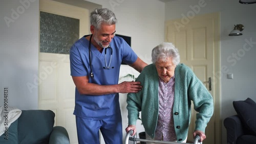 Caregiver helping senior woman to walk with walker in her home. photo