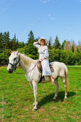 A serene and tranquil scene of a young woman riding a magnificent white horse in the golden glow of a sunlit summer day, with lush greenery in the background. © Ilja