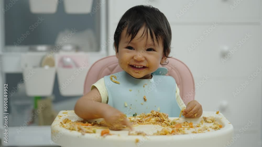 happy infant baby eating food and vegetable by self feeding BLW or baby led weaning on a chair happy infant baby eating food and vegetable by self feeding BLW or baby led weaning on a chair
