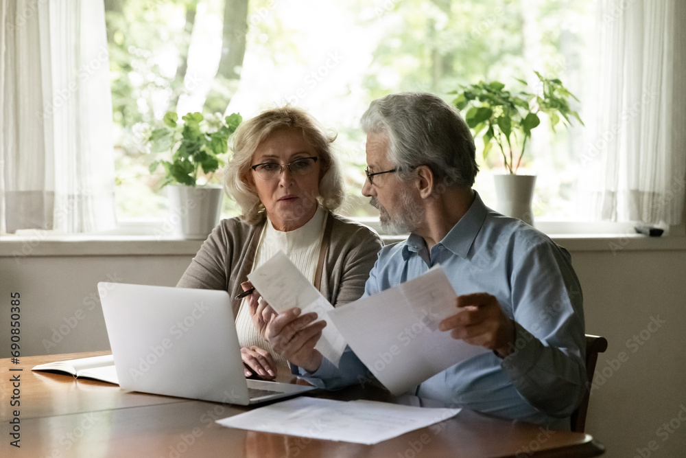 Seniors for paperwork. Serious aged family couple sit at table in home office review financial documents plan budget on future month discuss expenses. Mature spouses pay utility bills taxes online Seniors for paperwork. Serious aged family couple sit at table in home office review financial documents plan budget on future month discuss expenses. Mature spouses pay utility bills taxes online