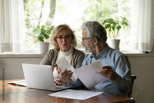 Seniors for paperwork. Serious aged family couple sit at table in home office review financial documents plan budget on future month discuss expenses. Mature spouses pay utility bills taxes online © fizkes