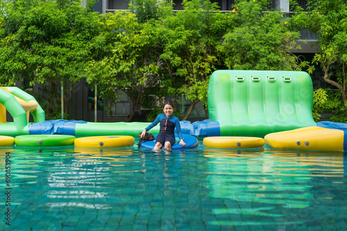 asian child swim or kid girl wearing swimsuit enjoy fun playing adventure water toys to Inflatable floating slider on swimming pool or waterpark and happy smile on holiday summer vacation at hotel