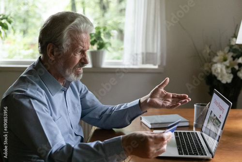 Fraud victim. Confused mature aged male online shopper look on computer screen overspending money unable to provide payment. Shocked middle aged man paid money to scammers get his credit card blocked photo