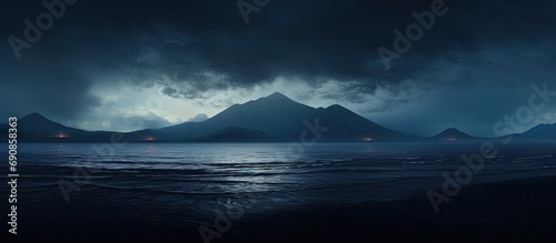 Volcanic beach with dark ocean water at sunset. Mountain silhouette with moody clouds at dusk.