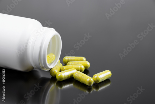 Yellow capsules and on a black background. Scattered pills on a dark background. Copy space. Pharmacy healthcare. White plastic bottle for pills