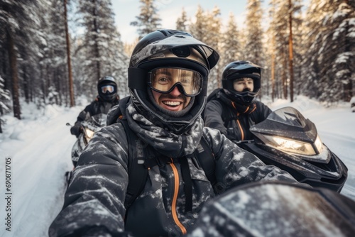 A group of young friends take a selfie while riding through a snowy forest on snow scooters. Active holiday in winter in the company of loved ones