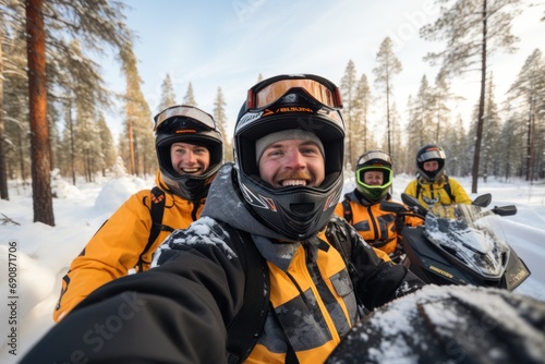 A group of young friends take a selfie while riding through a snowy forest on snow scooters. Active holiday in winter in the company of loved ones