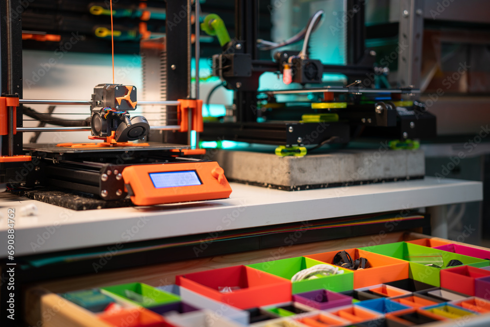 Home studio. 3D printers at work. Production, passion and hobby. Orange plactic filament. Drawer with printed elements. Order in the studio.