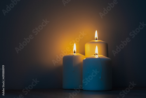 Three burning candles in the dark. Warm light from candles against cold dark background.