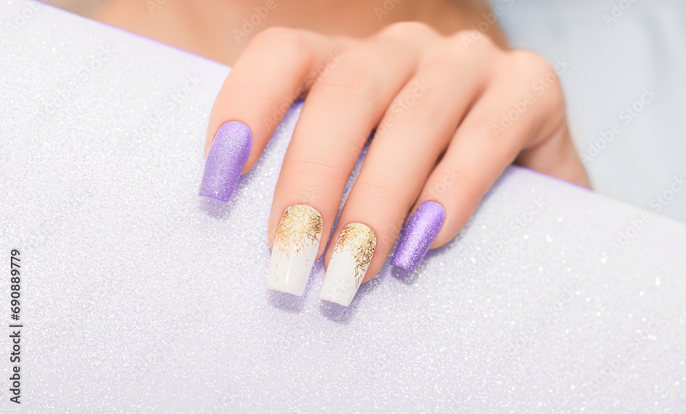 Female hands with long nails with glitter nail polish. Long purple and gold nail design. Women hand with sparkle manicure.