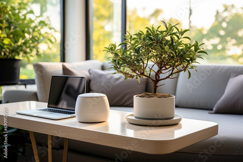 A warm and modern home office setup with a laptop, smart home device, and a bonsai tree on a desk near a window. © apratim