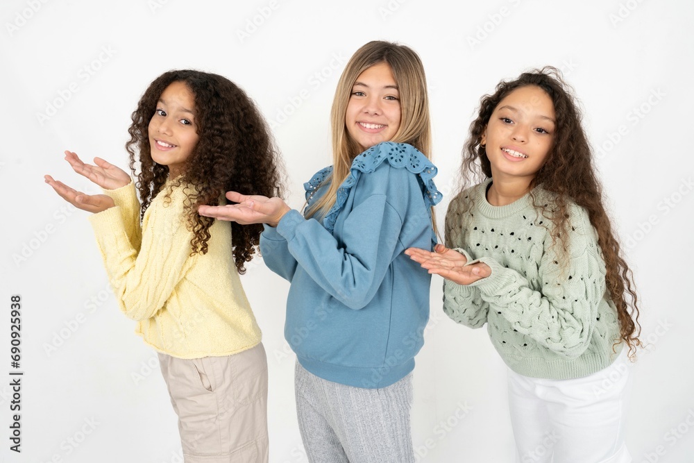 Three beautiful multiracial kid girls pointing aside with hands open palms showing copy space, presenting advertisement smiling excited happy Three beautiful multiracial kid girls pointing aside with hands open palms showing copy space, presenting advertisement smiling excited happy