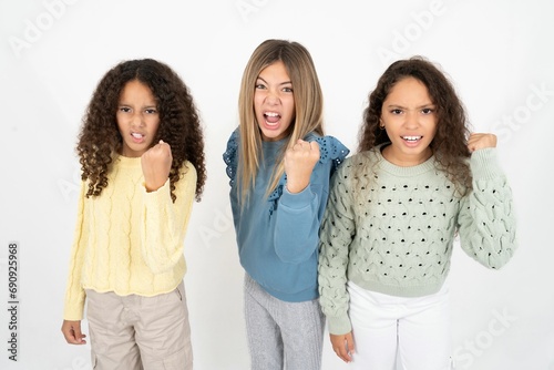 Three beautiful multiracial kid girls angry and mad raising fist frustrated and furious while shouting with anger. Rage and aggressive concept.