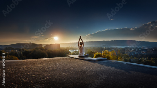 A woman practices yoga on the roof of a high-rise building at sunset.