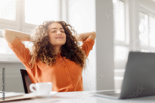 Relaxed curly-haired woman taking a break at desk, free space