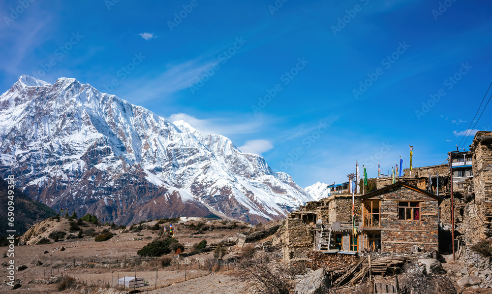 Stone houses with traditional Tibetan flags in a small village nestle at the base of the snow-clad Annapurna range