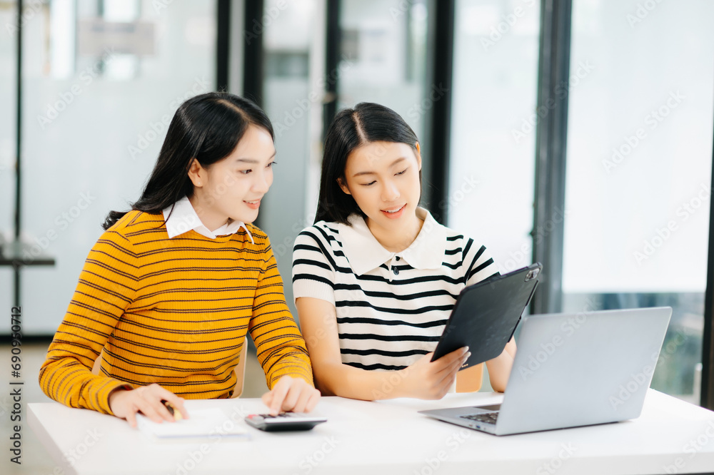 Two Attractive young Asian female college students working on the school project using laptop computer and tablet together, enjoy talking and snacking Two Attractive young Asian female college students working on the school project using laptop computer and tablet together, enjoy talking and snacking