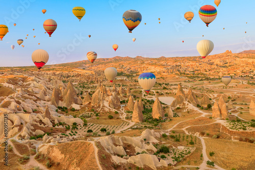 With their vibrant hues, hot air balloons ascend Cappadocian sky at dawn. Shed an enchanting glow on the distinctive summits beneath them in Goreme Rose Valley, a region of Cappadocia in Turkey.