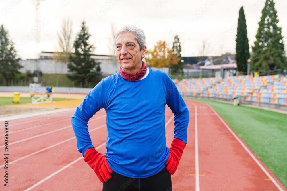 Fit elderly Caucasian man in blue enjoys a solo run on a cloudy day at an empty stadium. Fit elderly Caucasian man in blue enjoys a solo run on a cloudy day at an empty stadium.