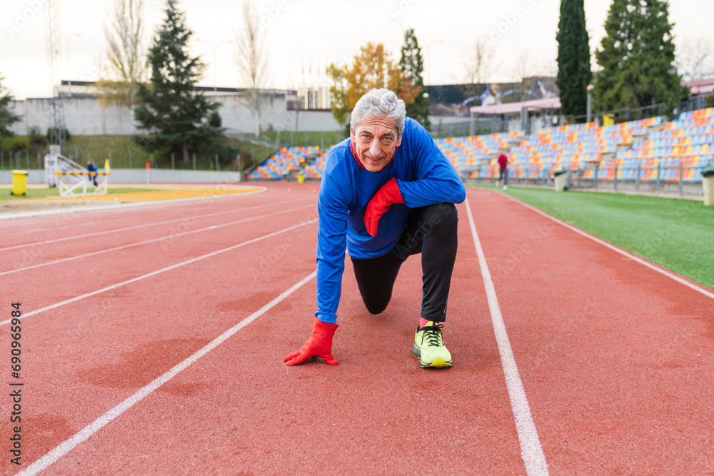 Obraz premium Aged Caucasian male athlete poised at start line on red racetrack, focused and ready to run.
