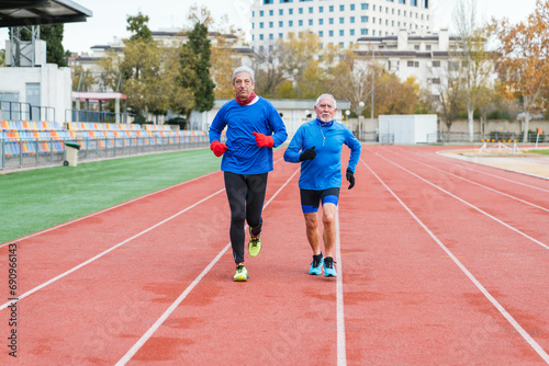 Two elder Caucasian men in sportswear running on an athletic track, focused and fit
