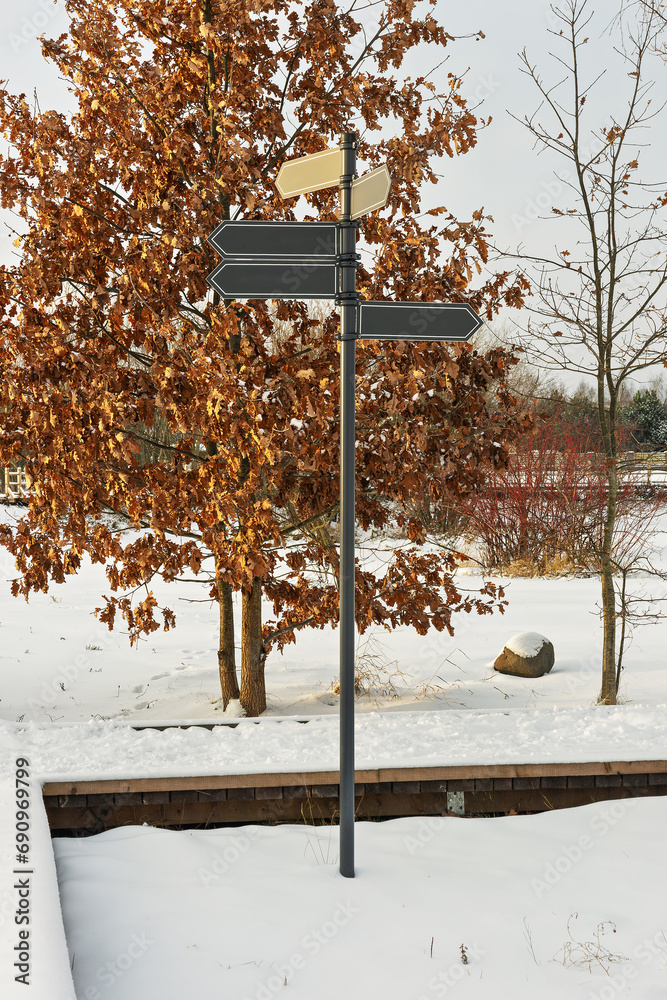 Naklejka premium Snow-covered Park with Arrows on Metal Pole in Winter Wonderland