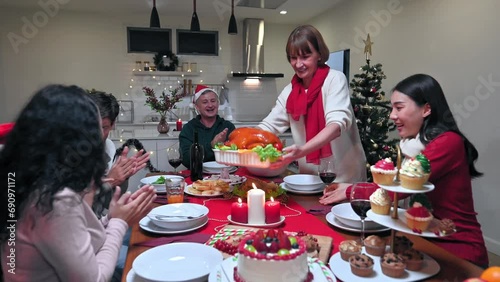 Big multi ethnic family enjoy eating celebrating together in a beautifully decorated dining room in christmas festival. Grandmother holding the dish baked turkey sharing to eating together on table. photo