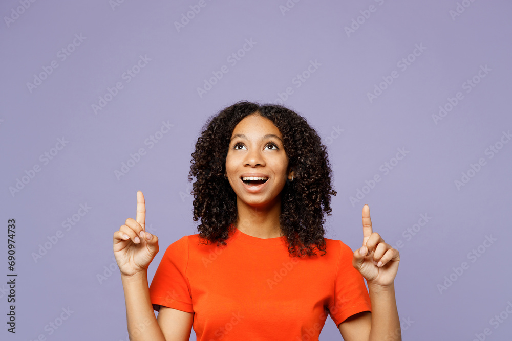 Little kid teen girl of African American ethnicity wears orange t-shirt point index finger overhead on area mock up isolated on plain pastel light purple background studio Childhood lifestyle concept Little kid teen girl of African American ethnicity wears orange t-shirt point index finger overhead on area mock up isolated on plain pastel light purple background studio Childhood lifestyle concept