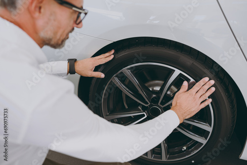 Cropped adult man customer male buyer client he wear shirt check touch wheel rim tire choose auto want to buy new automobile in car showroom vehicle salon dealership store motor show. Sales concept.