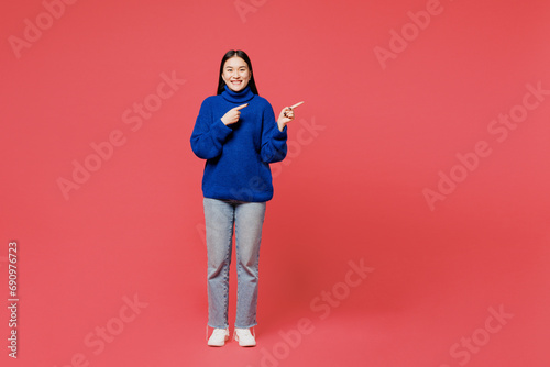 Full body young woman of Asian ethnicity wear blue sweater casual clothes point index finger aside on area mock up area copy space isolated on plain pastel pink background studio. Lifestyle concept. © ViDi Studio