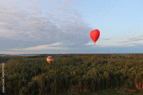 Two hot air balloons with people are flying over forests and fields in the morning at dawn