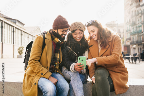 Friends sitting together using mobile phone to share content on social media in winter 