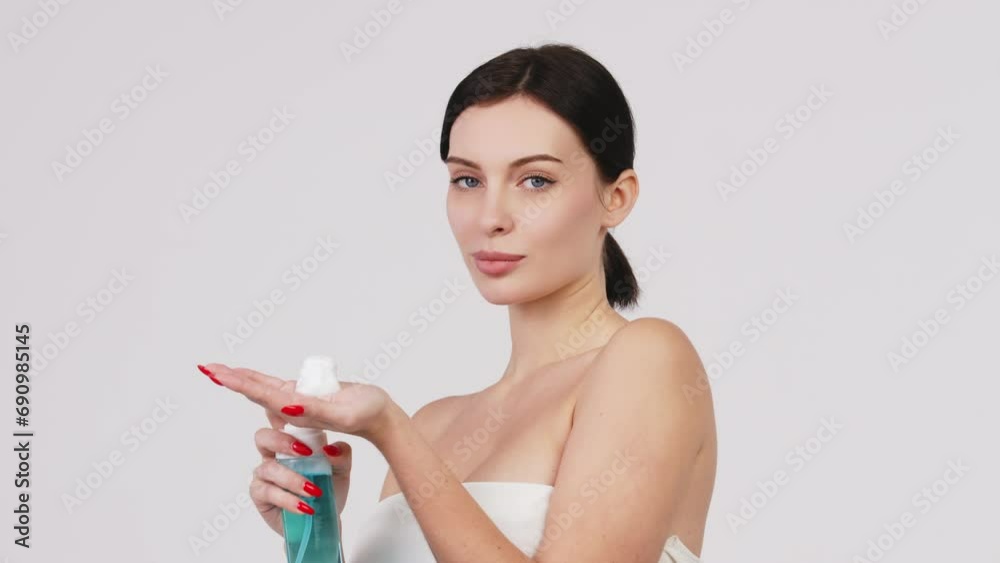 Cosmetology, hygiene, cleanliness. Close up portrait of beautiful young woman smiling holding bottle of gentle foaming facial cleanser isolated on light background Cosmetology, hygiene, cleanliness. Close up portrait of beautiful young woman smiling holding bottle of gentle foaming facial cleanser isolated on light background