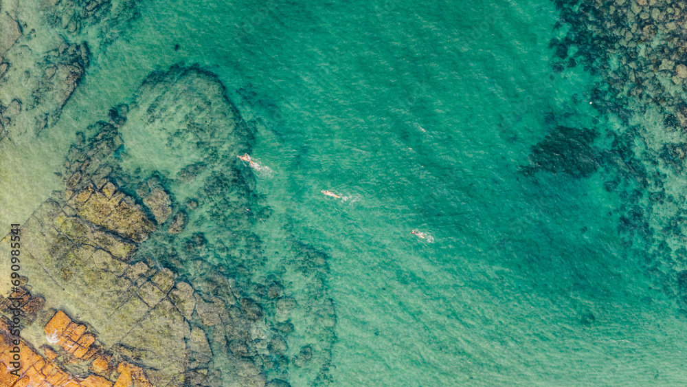 Aerial view from drone of people swimming in the middle of the sea of ​​turquoise green water, on a quiet Sydney beach in the reefs and corals