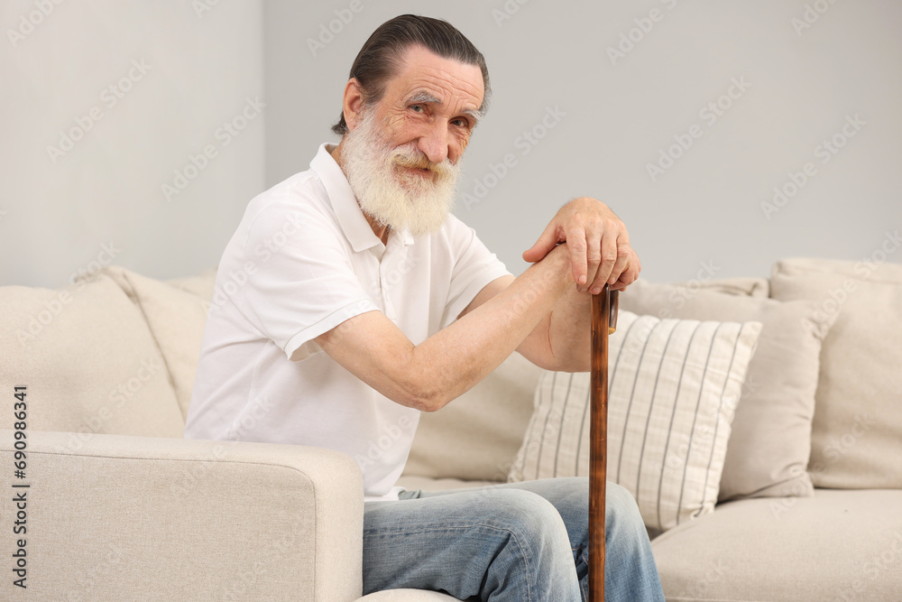 Senior man with walking cane on sofa indoors