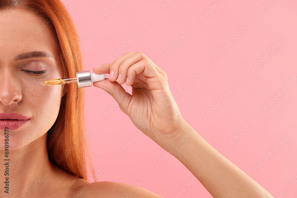Beautiful young woman applying cosmetic serum onto her face on pink background, closeup. Space for text