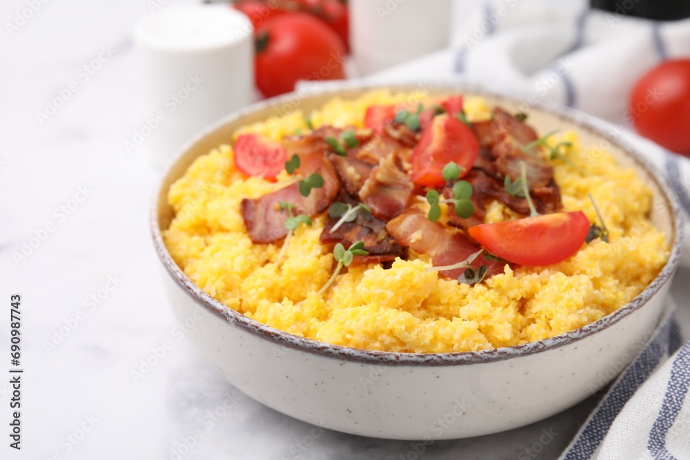 Tasty cornmeal with tomatoes, bacon and microgreens in bowl on white table, closeup. Space for text Tasty cornmeal with tomatoes, bacon and microgreens in bowl on white table, closeup. Space for text