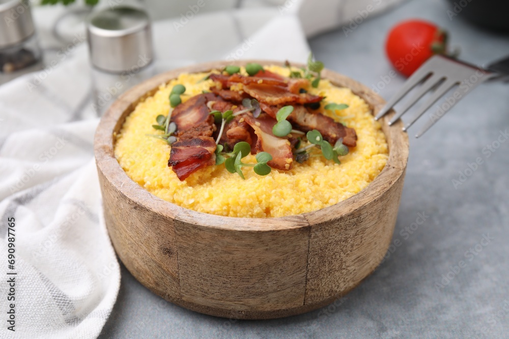 Cooked cornmeal with bacon and microgreens in bowl on light grey table, closeup Cooked cornmeal with bacon and microgreens in bowl on light grey table, closeup