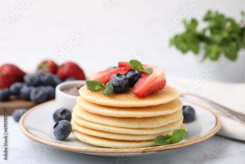 Delicious pancakes with strawberries, blueberries and chocolate sauce on light table, closeup